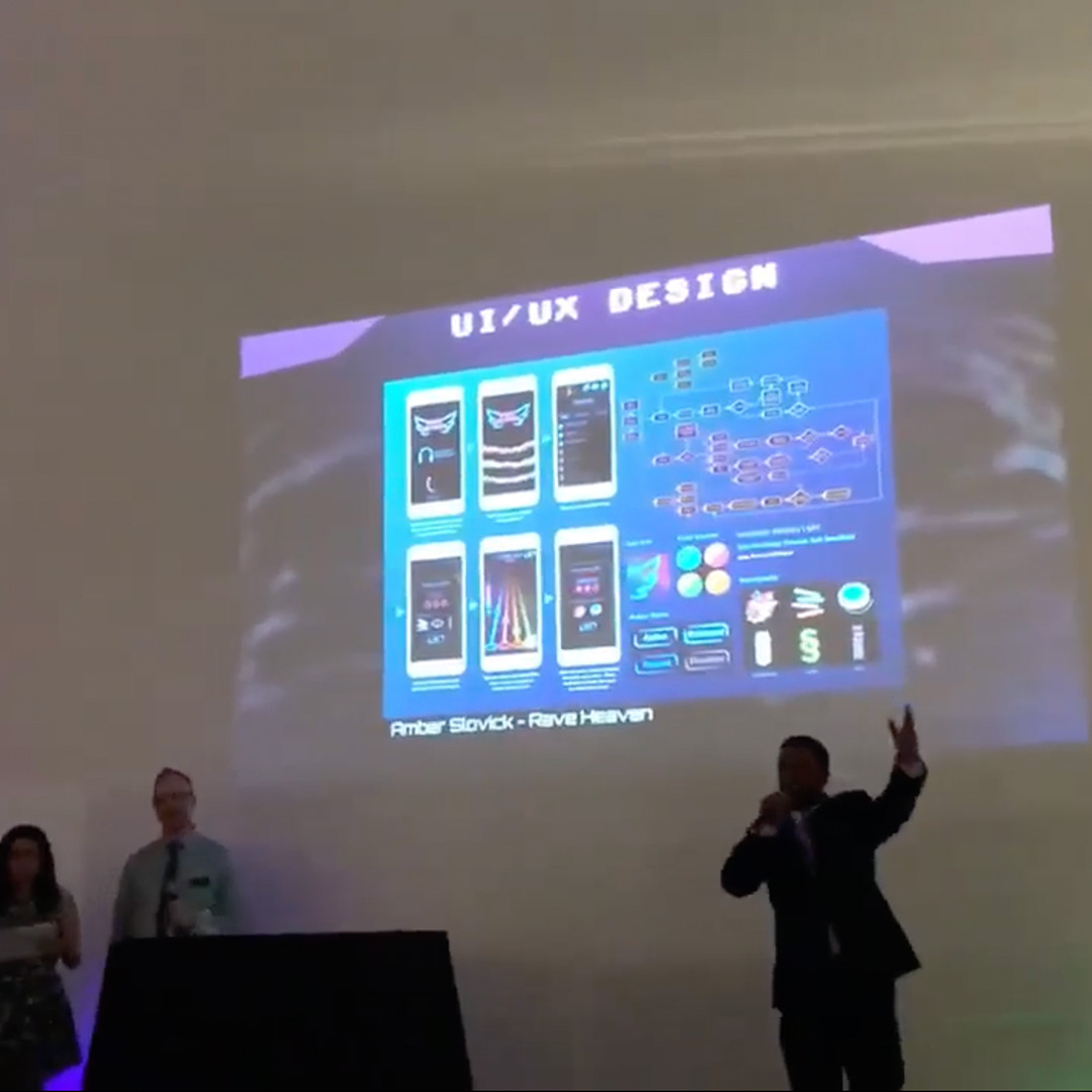 A man with a microphone standing in front of a projected screen that says: UI/UX Design: Amber Slovick - Rave Heaven